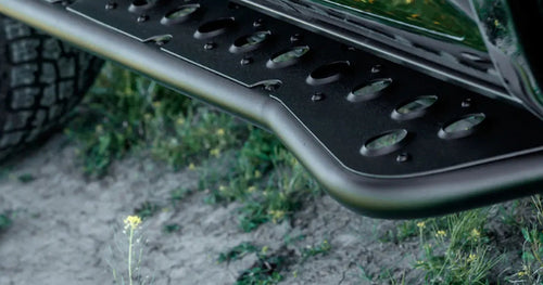 Black Cali Raised LED Step Edition rock slider with a perforated top plate installed on a Toyota 4Runner, above grass and dirt
