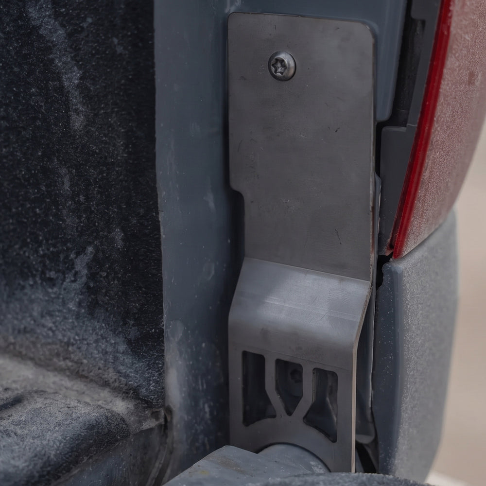Cali Raised LED tailgate theft protector installed at the passenger-side tailgate hinge of a 2014-2021 Toyota Tundra, secured with one supplied security bolt. Current protector shown; no CR cutout.