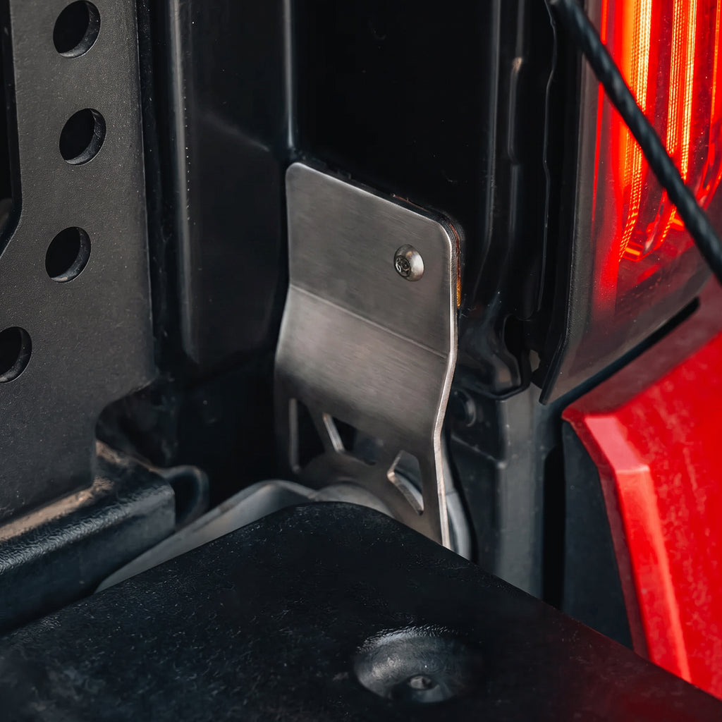 Earlier CR-cutout protector installed at the Tacoma passenger-side tailgate hinge. Current protector has no CR cutout; installation is unchanged.