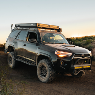 Black Toyota 4Runner with a rooftop tent, ALWD-equipped roof rack, and off-road gear driving on a trail