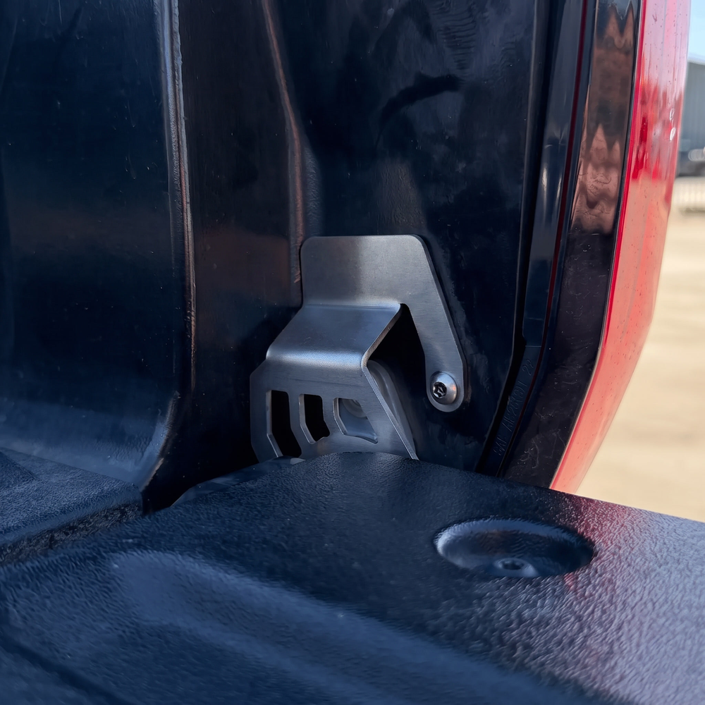 Cali Raised LED tailgate theft protector installed at the passenger-side tailgate hinge of a 2022+ Toyota Tundra, secured with one supplied security bolt. Current protector shown; no CR cutout.