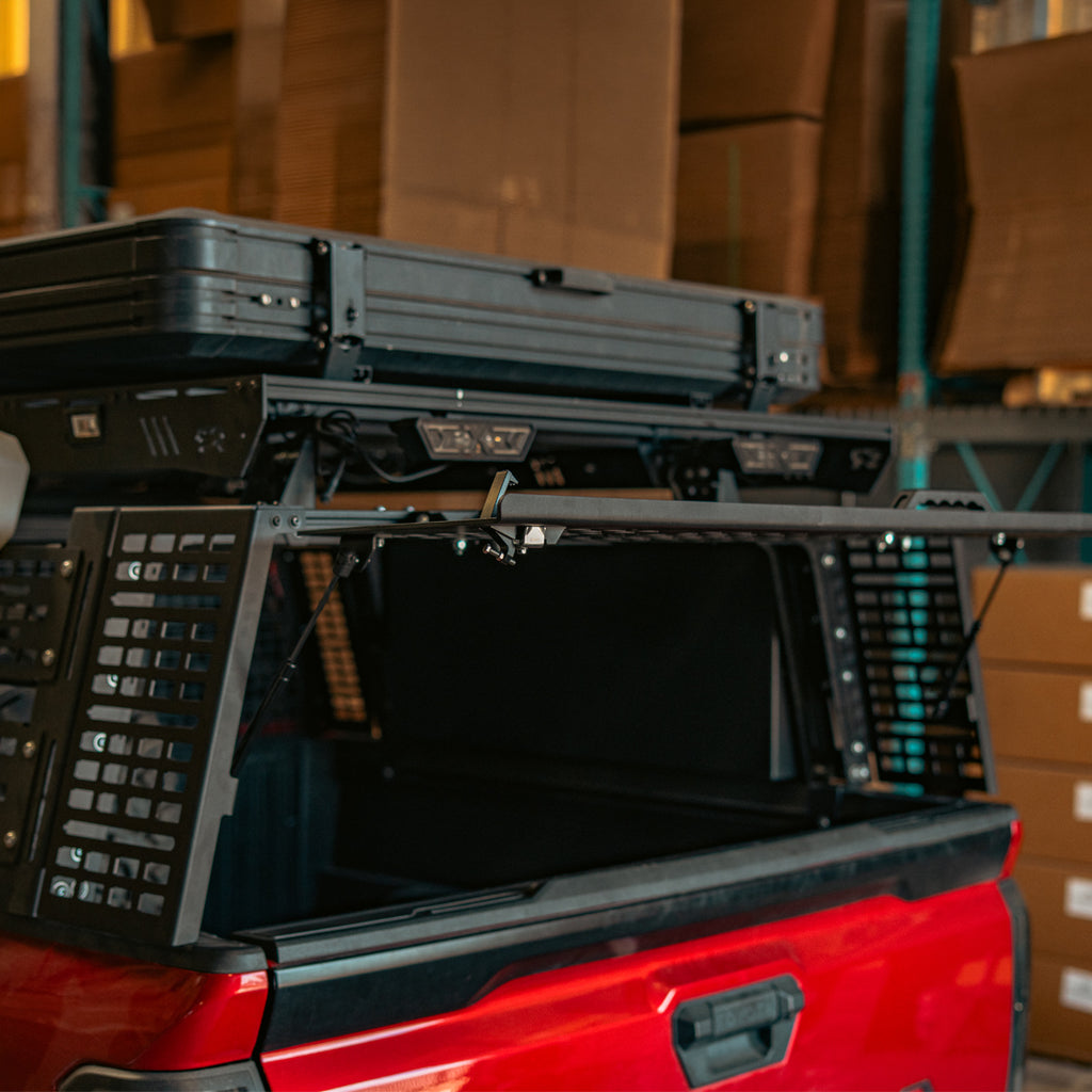 Rear hatch lifted open over the bed of a red Toyota Tacoma overland bed rack