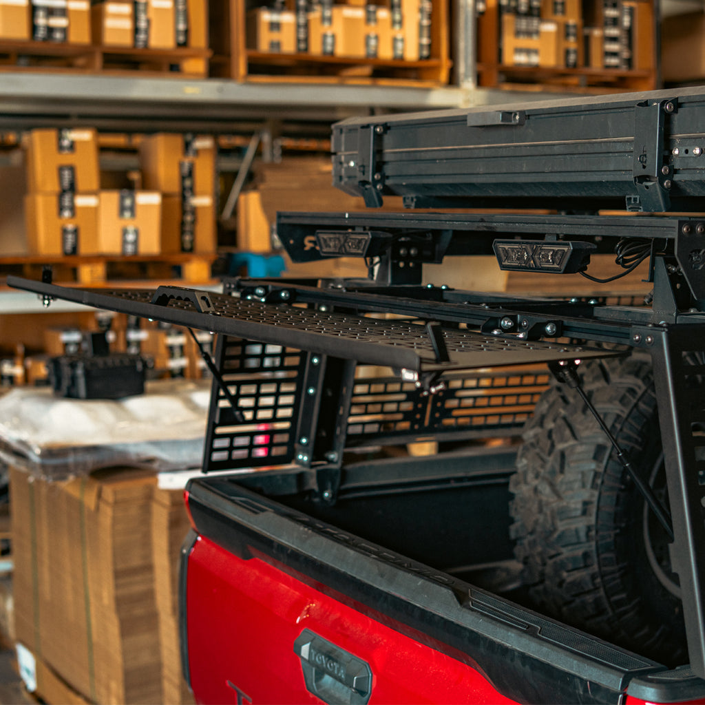 Open rear hatch on a Toyota Tacoma overland bed rack showing access to the truck bed