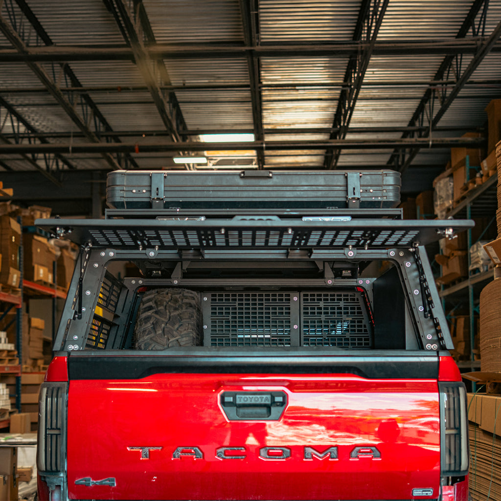 Overland bed rack rear hatch on a red Toyota Tacoma, viewed from behind with the hatch open