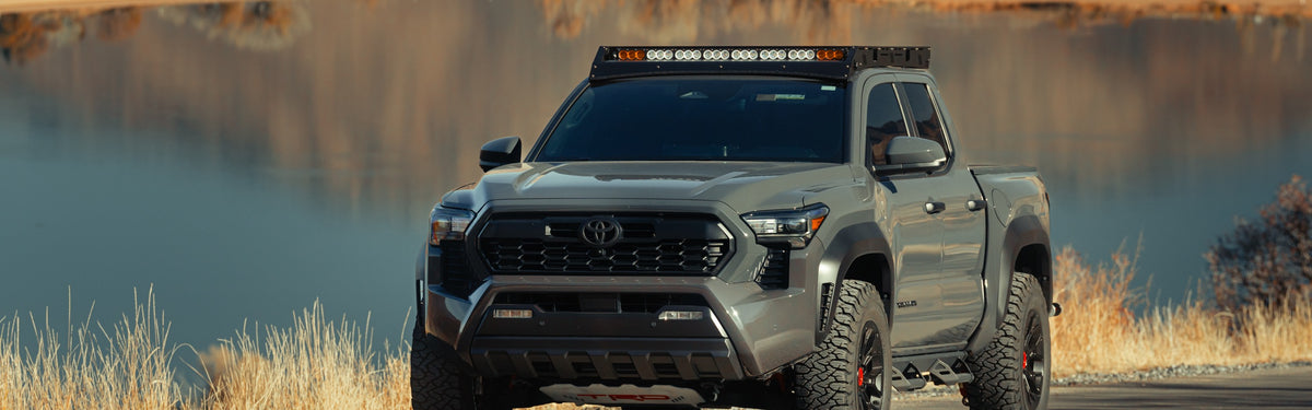 Toyota Tacoma with a Cali Raised roof rack and LED light bar parked beside a mountain lake