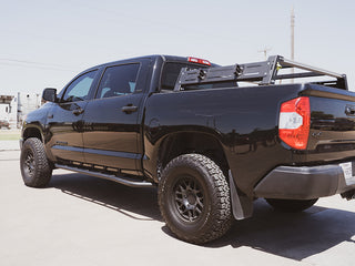A black 2014–2021 Toyota Tundra equipped with a mid-height Cali Raised LED Overland Bed Rack, showcasing its off-road setup.